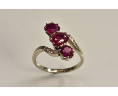 A ruby and diamond twist ring, central oval pinky red ruby, flanked by a smaller round cut ruby either side, between diamond 