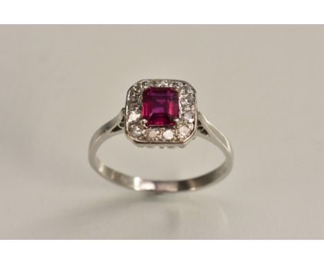 A ruby and diamond cluster ring, central rectangular baguette cut ruby, approx 0.63ct, surrounded by a band of twelve round b