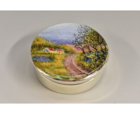 A George V silver and enamel circular rouge box, hinged cover decorated in polychrome with a cottage in a winding country lan