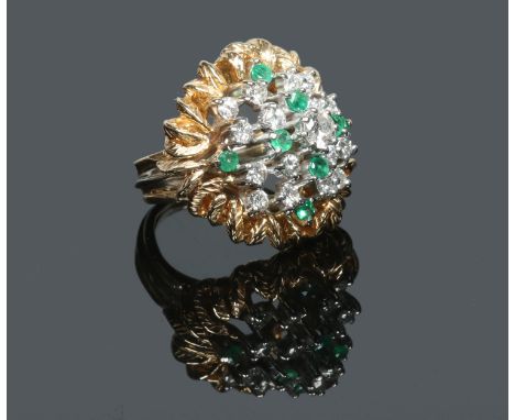 A 14 carat gold emerald ruby and diamond cluster ring. Set on a bezel of leaf scrolls and with a reeded shank. The principal 