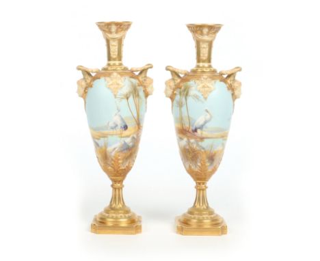 A pair of Royal Worcester twin handled pedestal vases by William Powell. Each moulded with masks, ground in pale matt blue an