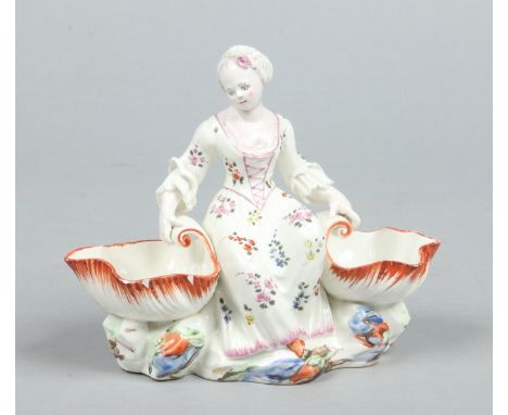 A Mennecy figural sweetmeat dish coloured in enamels. Formed as a maiden seated between two shells and raised on a rockwork b