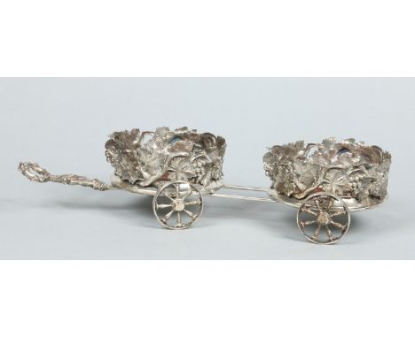 A silver plated novelty two bottle decanter stand in the form of a cart and with steerable front axle. Decorated with natural