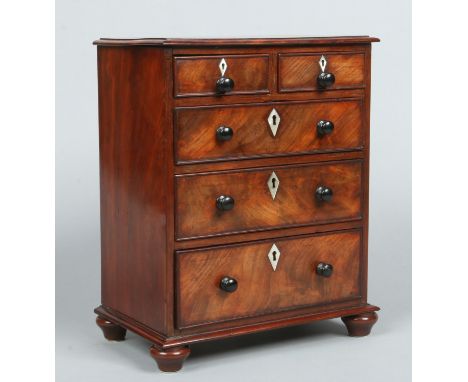 A 19th century figured mahogany miniature chest of two over three drawers, the bottom drawer as a two compartment tea caddy. 