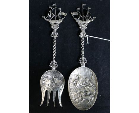 A Dutch embossed silver (.833 min) serving spoon, with tavern scene to bowl and sailing ship finial and a similar fork