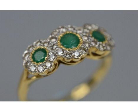 A MODERN 18CT GOLD EMERALD AND DIAMOND TRIPLE CLUSTER RING, head measuring approximately 18.0mm x 8.5mm, estimated total diam