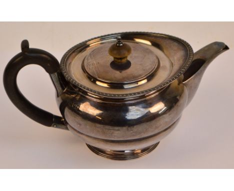 A George V hallmarked silver teapot of squat circular form with cast decorated rim, turned wooden finial to the lid with flus