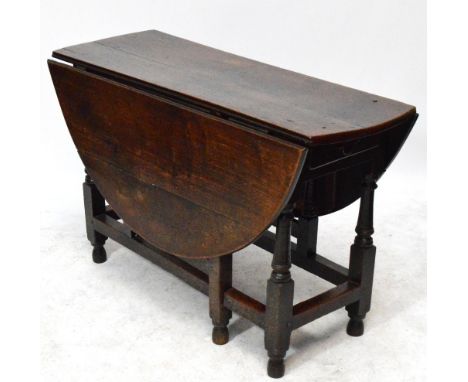 An 18th century oak gateleg drop leaf dining table with twin rounded flaps and raised on ring turned block supports united by