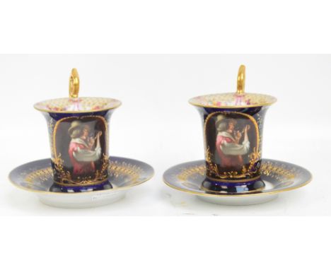 A pair of Vienna transfer decorated chocolate cups and saucers with high scrolling gilt loop handles on a blue ground, each c