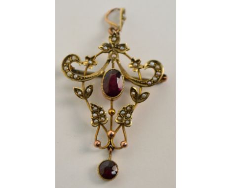 An Edwardian 9ct yellow gold pierced scrolling pendant set with seed pearls and centred on an oval garnet with a round garnet