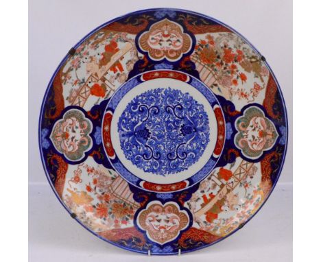 A large Japanese Meiji period circular charger in Imari pattern with panels of figures and flowers with central blue and whit