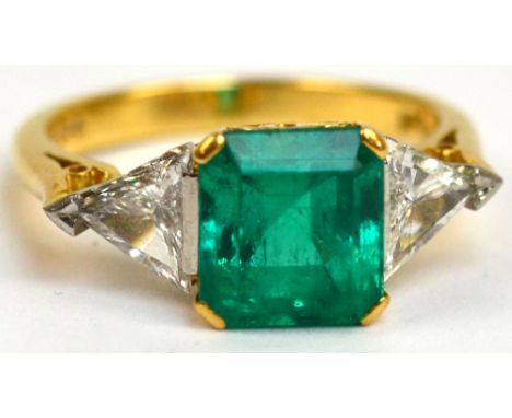 An 18ct yellow gold emerald and diamond ring, the central square stone in high pierced claw setting, flanked by two trillion 