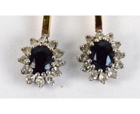 A pair of yellow metal sapphire and diamond cluster earrings with small diamond chips surrounding the central oval sapphire a