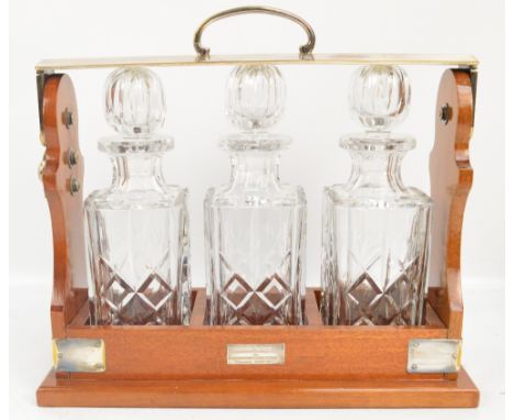 A mahogany and silver plate mounted three bottle tantalus with engraved presentation plaque, three cut glass decanters with l