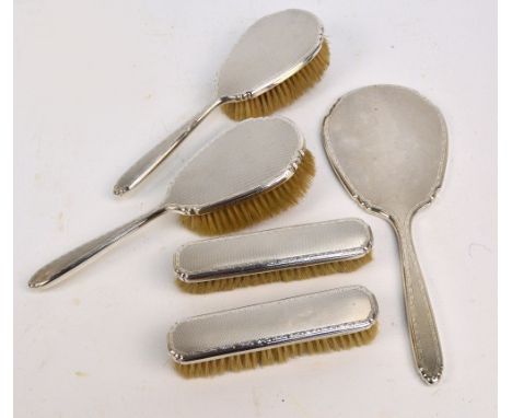 A George VI hallmarked silver backed five piece dressing table set with overall engine turned decoration within a foliate bor