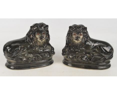 A pair of c.1900 ceramic figures of recumbent lions with glass inset eyes on oval bases, width 28cm. CONDITION REPORT: Two sm