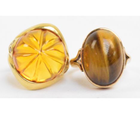 A yellow metal dress ring set with oval tiger's eye cabochon, size O and a further yellow metal dress ring with amber coloure