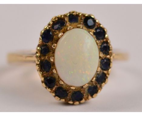 A 9ct yellow gold cluster ring set with oval opal in claw setting within a border of small blue stones, size N, approx 3.8g.