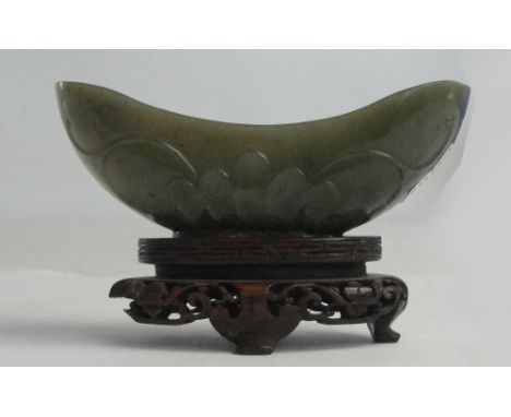 A Chinese jade oblong bowl with raised ends and carved stylised tendril decoration to the outside, length 10cm, on carved har
