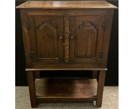 A Titchmarsh and Goodwin style oak cupboard on stand, over-sailing rounded rectangular top, pair of cupboard doors enclosing 