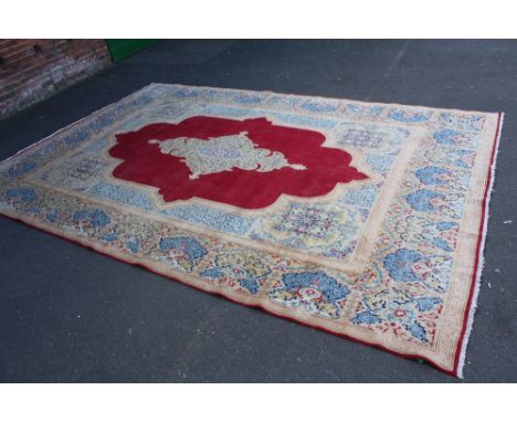 AN EASTERN EARLY 20TH CENTURY WOOLLEN RUG / CARPET, the central shaped cartouche within a red shaped border lighter yellow al