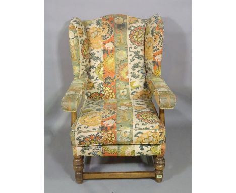 A 20th century oak framed wingback open armchair on ring turned supports and floral upholstery. 
