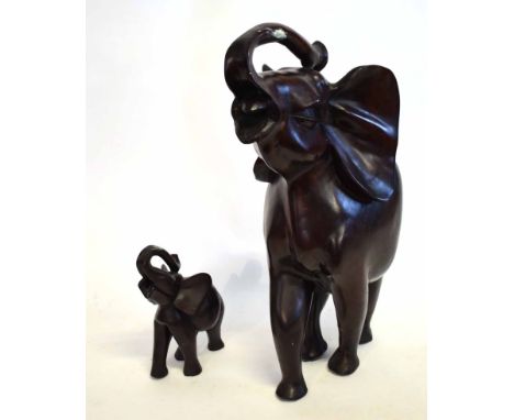 Large Eastern hardwood carved model of an elephant with raised trunk, together with a further smaller example, largest 87cms 