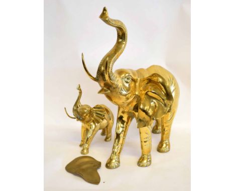 Large brass model of an elephant with raised trunk and damage to ear, together with a further smaller example, largest 70cms 