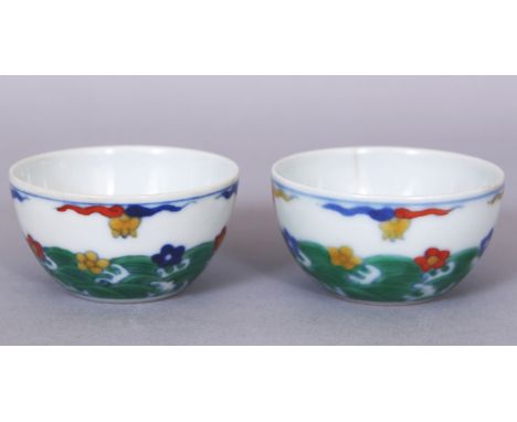 A SMALL PAIR OF CHINESE DOUCAI PORCELAIN WINE CUPS, each decorated with stylised waves bearing flowerheads, each base with a 