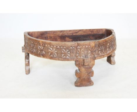An Indian hardwood corn grinder, of demi lune form, the outer frieze carved with repeating geometric stars, raised upon three
