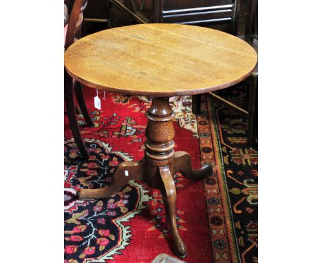 A George III oak tripod table, the circular five plank top raised upon a baluster pedestal, three down swept supports and pad