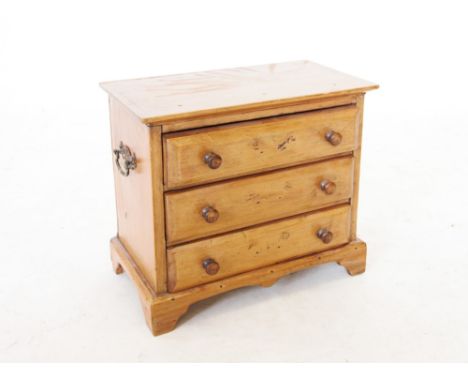 A Victorian pine apprentice chest, with three long drawers, applied with hardwood button handles and brass side swing handles