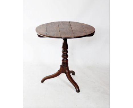A George III oak tripod table, the circular tilting plank top raised upon a knopped baluster pedestal and three down swept su