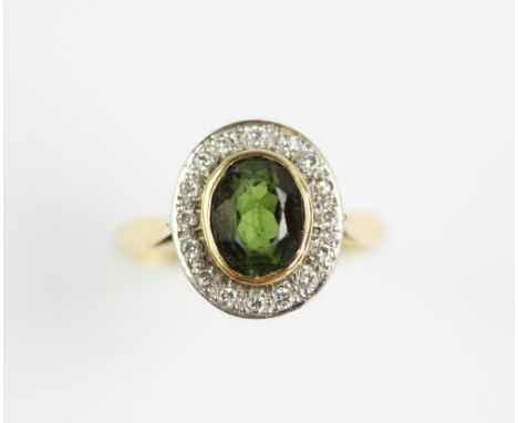 A peridot and diamond cluster ring, designed as a central oval peridot, collet set in yellow gold, within a diamond set surro