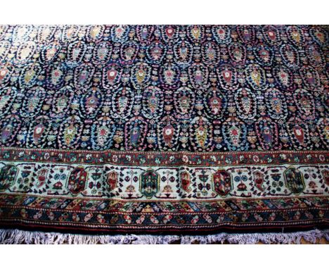 A large Caucasian pattern wool carpet, the central panel with repeating multi coloured guls on a navy blue ground, within a c