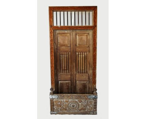 A Rajasthani rustic hardwood balcony door, with an iron bar grille above a pair of panelled doors, within a frame carved with