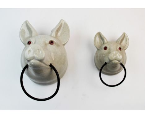 A graduated pair of continental ceramic towel rails, 20th century, modelled as pig masks, the craquelure glaze set with glass