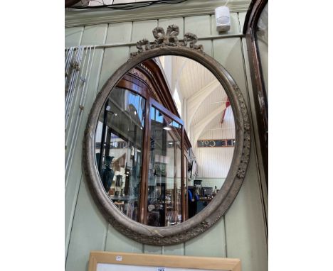 Oval framed wall mirror with ribbon crest, 97cm by 69cm.