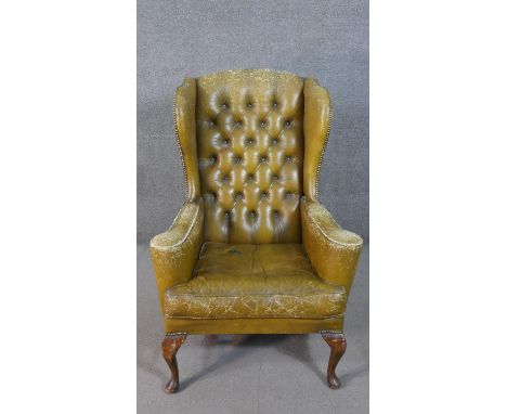 A wing back armchair, upholstered in green leather, with a button back, on cabriole legs, joined by turned H stretchers. 