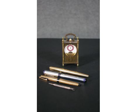 A Schild eight day miniature carriage clock with open escapement and enamel dial along with four vintage pens, including a Sc