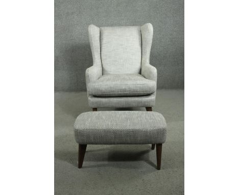 A contemporary wing back armchair and foot stool, upholstered in light grey fabric, on tapering cylindrical wood legs. 