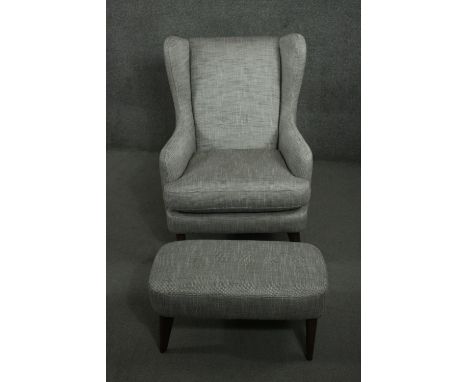 A contemporary wing back armchair and foot stool, upholstered in light grey fabric, on tapering cylindrical wood legs. 