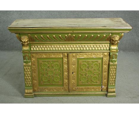 A green painted and parcel gilt cabinet, with a gadrooned cornice, above a frieze of scales, over two carved doors, flanked b