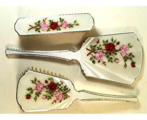 A hallmarked silver and enamel three piece dressing table setDecorated with roses on an ivory ground, made by HCD, Birmingham