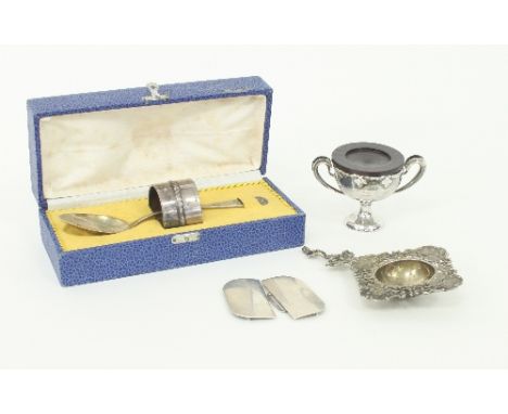 A German silver .800 standard napkin ring and spoon, a sterling silver buckle, a tea strainer and a two handled cup and stand