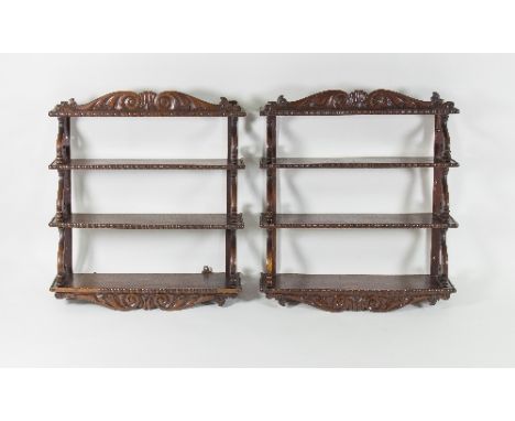 A fine pair of late Regency mahogany hanging shelves, with foliate pediment and moulded borders to the shelves, on scroll sup