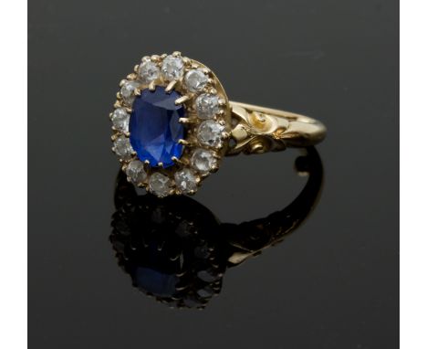 A sapphire and diamond cluster ring, claw set with an oval shaped sapphire within a frame of cushion shaped diamonds