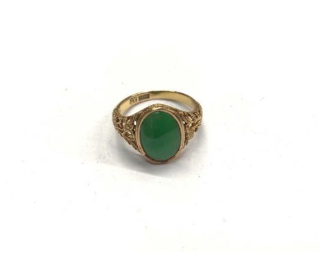 18ct gold green hard stone oval panel ring with carved floral scroll shoulders, size MShank stamped 18K. Weight 3.6 gramsThe 