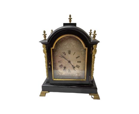 A late 19th/early 20th century ebonised and cast brass mounted mantle clock. The arched case sumounted by 5 flaming urn finia