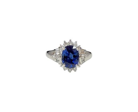 A platinum sapphire and diamond cluster ring, an oval sapphire with round brilliant cut diamond surround to tapered baguette 